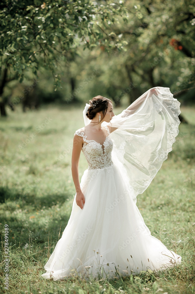 bride posing in a green park; girl in a white dress on a background of green