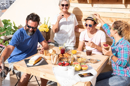 Four people smiling together and one dog. Caucasian family with parents  teenager son and grandmother. Wooden table with homemade cakes  fruit and coffee.