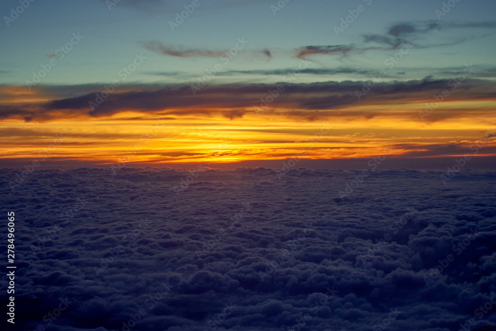 orange sky and clouds from an airplane window during an evening flight.