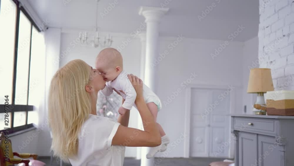parental kiss, young mother raises above the head in slow motion of the sweet newborn girl with finger in mouth parental kiss, young mother raises above the head in slow motion of the sweet newborn girl with finger in mouth