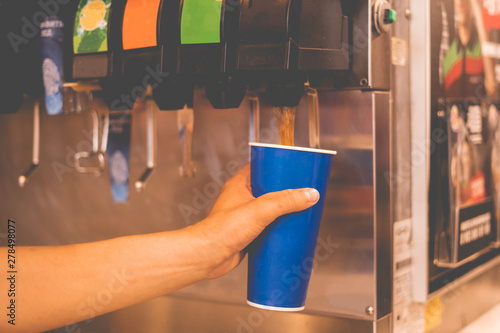 hand holding a paper glass to pour the lemonade soda soft drink  machine  in a fastfood restaurant