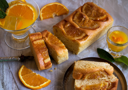 fruchtiger rührkuchen mit orangenscheiben belegt, mit einem glas orangensaft und einem orangenlikör