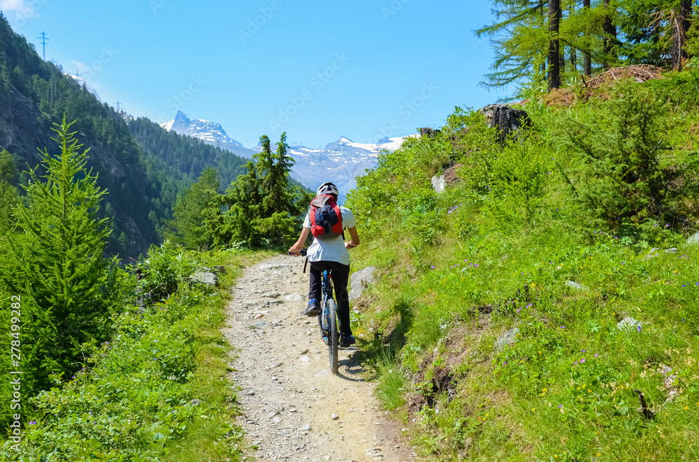 Young man riding bicycle in beautiful hilly landscape of Swiss Alps close to famous Zermatt. Outdoor sport. Bike, biker. Alpine landscape, Switzerland. Mountains with snow on top in background