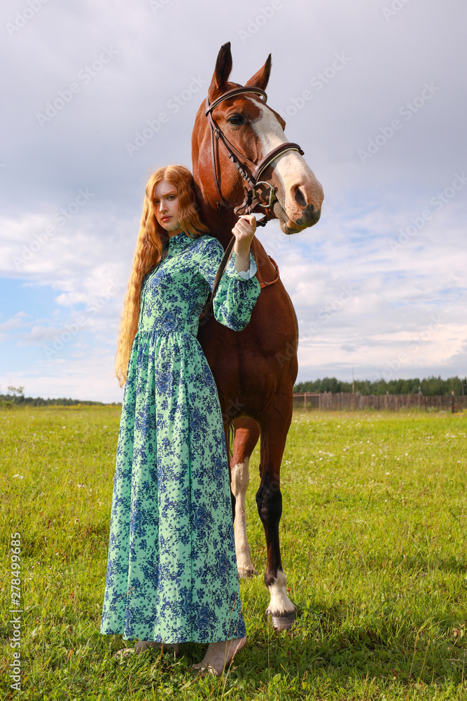 Fototapeta premium orange hair woman and her brown horse in the field just relaxing in summer day