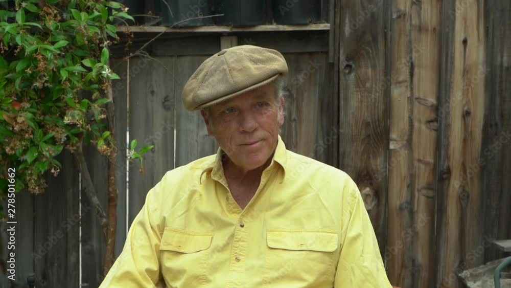 Senior retired male portrait with serious face, camera zooming in, wearing Scottish hat and yellow shirt, outdoor backyard, slow motion Senior retired male portrait with serious face, camera zooming in, wearing Scottish hat and yellow shirt, outdoor backyard, slow motion
