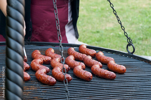 Many tasty sizzling sausages on the outside grill, springtime barbecue party in the yard, bbq concept, a person in an apron roasting the delecious greasy sausages, green grass lawn in the background photo