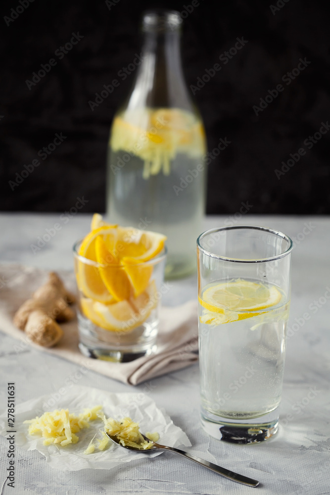 Homemade refreshing infused detox water or lemonade in glass bottles with grated ginger and lemon on dark background close-up with copy space for text.Healthy vegan drink concept.Selective focus Homemade refreshing infused detox water or lemonade in glass bottles with grated ginger and lemon on dark background close-up with copy space for text.Healthy vegan drink concept.Selective focus
