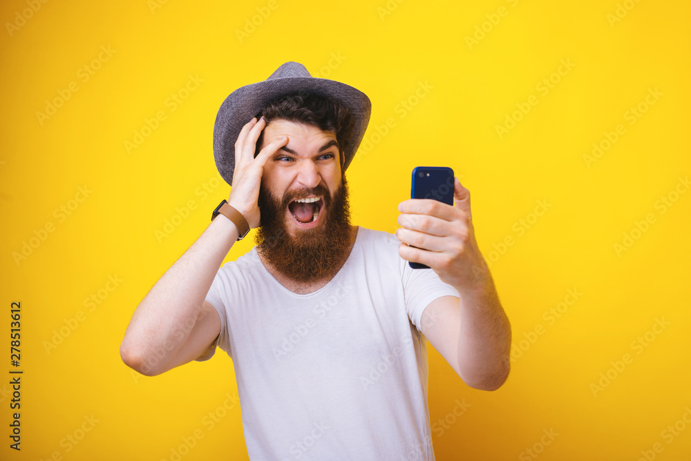 Photo of handsome bearded guy, holding mobile phone and looking amazed at sreen, over yelow background Photo of handsome bearded guy, holding mobile phone and looking amazed at sreen, over yelow background