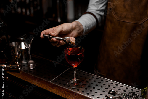 Professional bartender putting a rose bud to the red cocktail in the glass