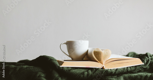 A Cup of warm drink and a book with pages folded into a heart on a cozy knitted blanket.