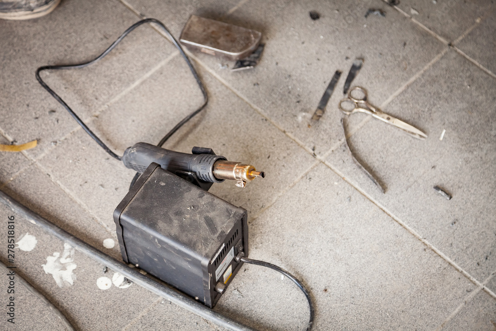 Industrial soldering gun of black color on the floor among dust and tools for heating and melting plastic during the connection of parts in the workshop for repair and restoration of car bumpers