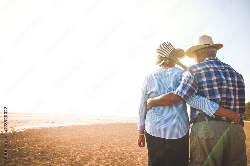 An elderly Asian couple standing hugging each other at the beach, seeing the evening light.