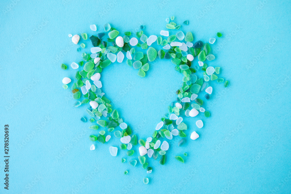 Close up of various sea glass pieces in the shape of a heart on blue background. Design template. Frame with copy space for text. Top view, flat lay