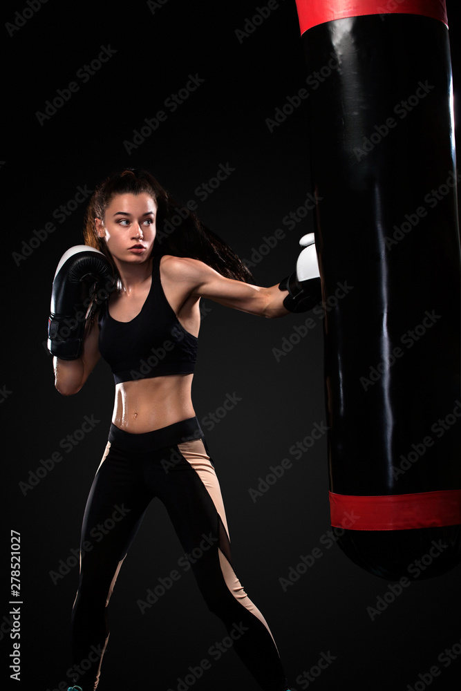 Woman boxer fighting in gloves with boxing punching bag on black background. Boxing and fitness concept. Woman boxer fighting in gloves with boxing punching bag on black background. Boxing and fitness concept.