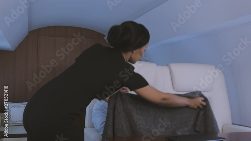 Stewardess taking care of passenger. Biracial flight attendant covering tired sleepy businessman with blanket during trip on private business jet.