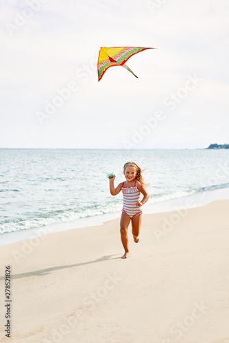 Happy child girl with a kite running on tropical beach