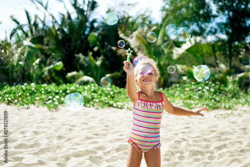 Little happy girl playing soap bubbles on the topical beach