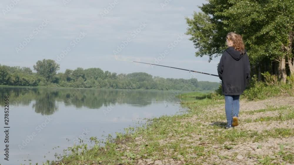 cute teenag girl fishing on river bank standing on the sand and holding fishing rod. cute teenag girl fishing on river bank standing on the sand and holding fishing rod.
