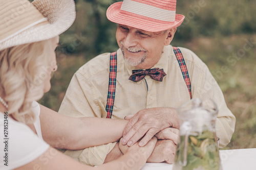 Happy relationship of an old couple. Smiling little old grandparents are sitting at the table and talking about the memories of youth. Drink lemonade with fruit in the garden