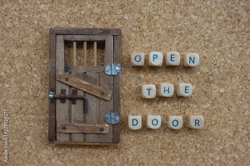 Open the door concept with a composition of wooden dice letters and a door miniature over a cork board