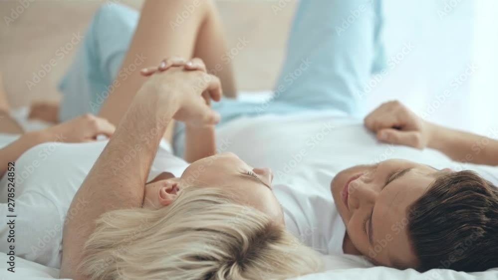 overhead view of couple lying in bed, holding hands, smiling and kissing at home overhead view of couple lying in bed, holding hands, smiling and kissing at home