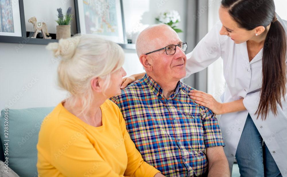 Obraz premium Smiling nurse talking with senior couple during home visit