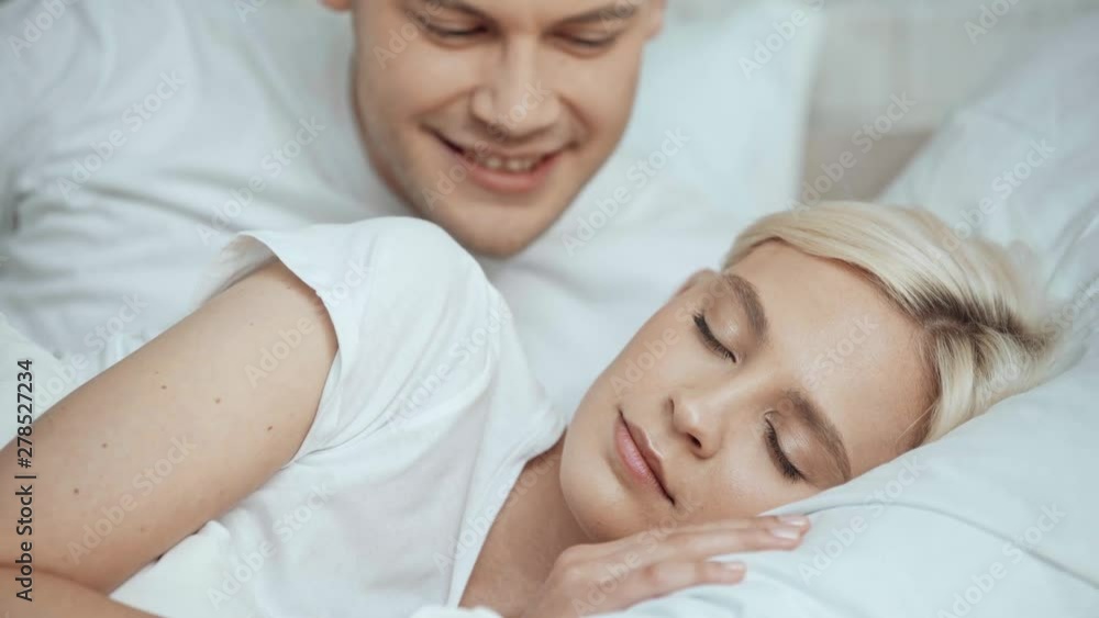 handsome man embracing and waking up beautiful sleeping woman with kissing in bed handsome man embracing and waking up beautiful sleeping woman with kissing in bed
