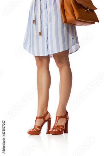 Brown women's shoes and leather bag. Beautiful female legs wearing summer high heeled sandals in blue dress and brown woman handbag on white background.