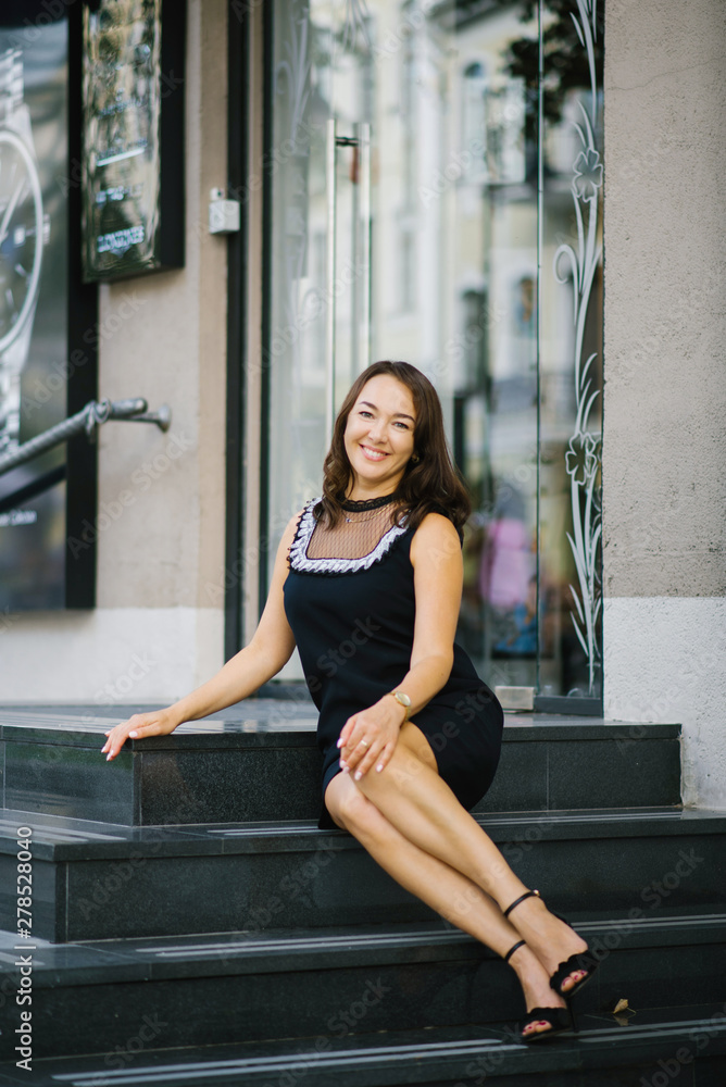 Portrait of a beautiful mature woman sitting outdoors on wide marble or granite steps looking smiling and feeling happy	