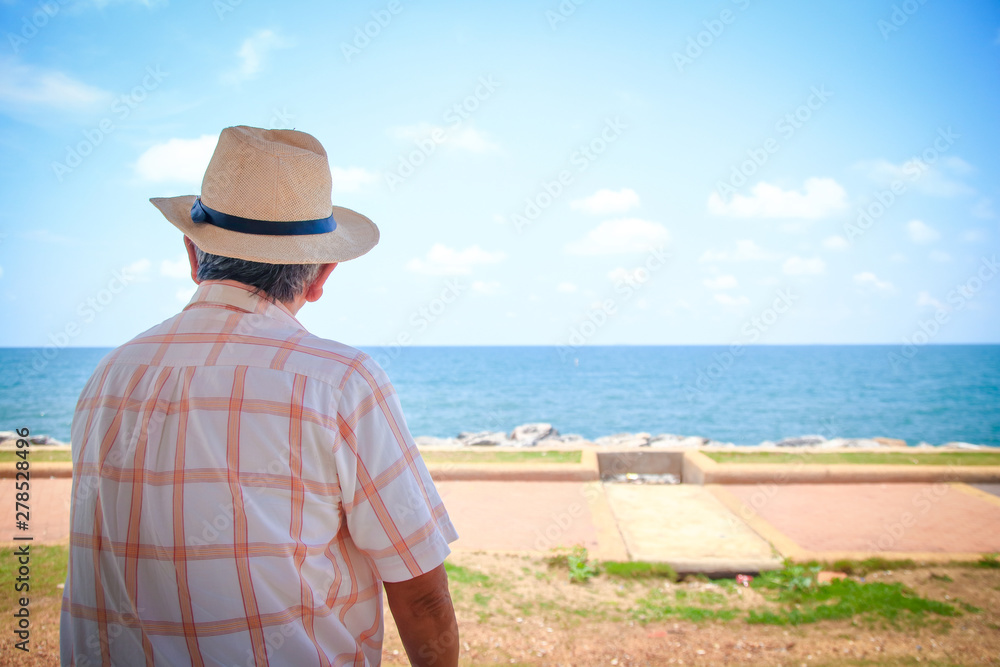 An elderly man wearing a hat looking at the beautiful sea