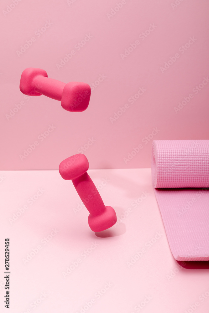 pink bright dumbbells levitating in air near rubber fitness mat on pink background pink bright dumbbells levitating in air near rubber fitness mat on pink background