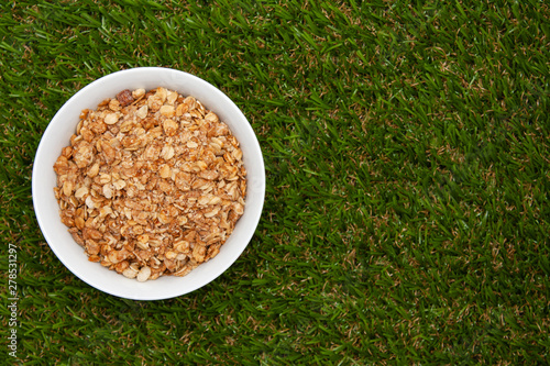 Muesli with banana in a white bowl on green grass with copyspace