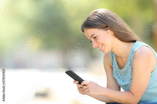Happy woman checking phone online content in a park