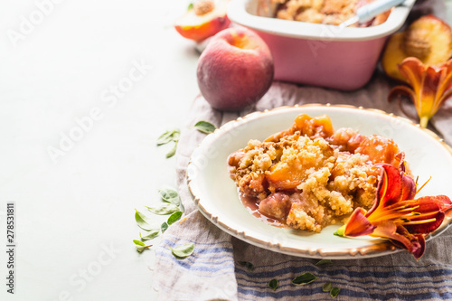 Close up of delicious peach cobbler  dessert in plate on light background with baking pan and fresh peaches . Copy space