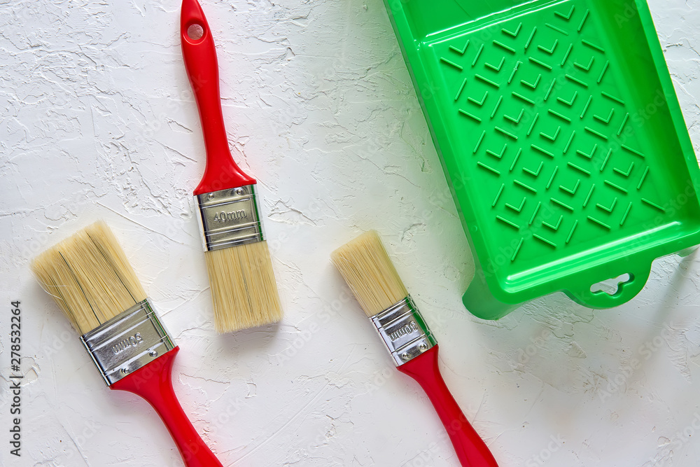 Three brushes with red handles and green paint tray on white concrete background. tools and accessories for home renovation. Top view