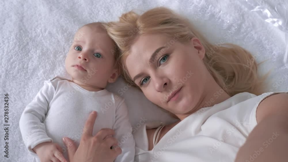relationship child and mother, young parent with a sweet infant girl lying on the white bed and pose on camera close up relationship child and mother, young parent with a sweet infant girl lying on the white bed and pose on camera close up