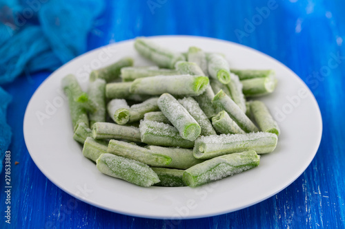 frozen green beans on white plate on ceramic background