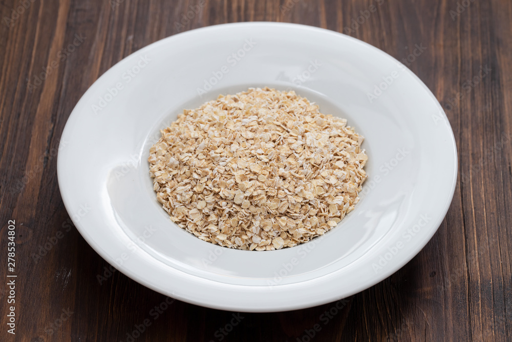 uncooked oats in white plate on wooden background uncooked oats in white plate on wooden background
