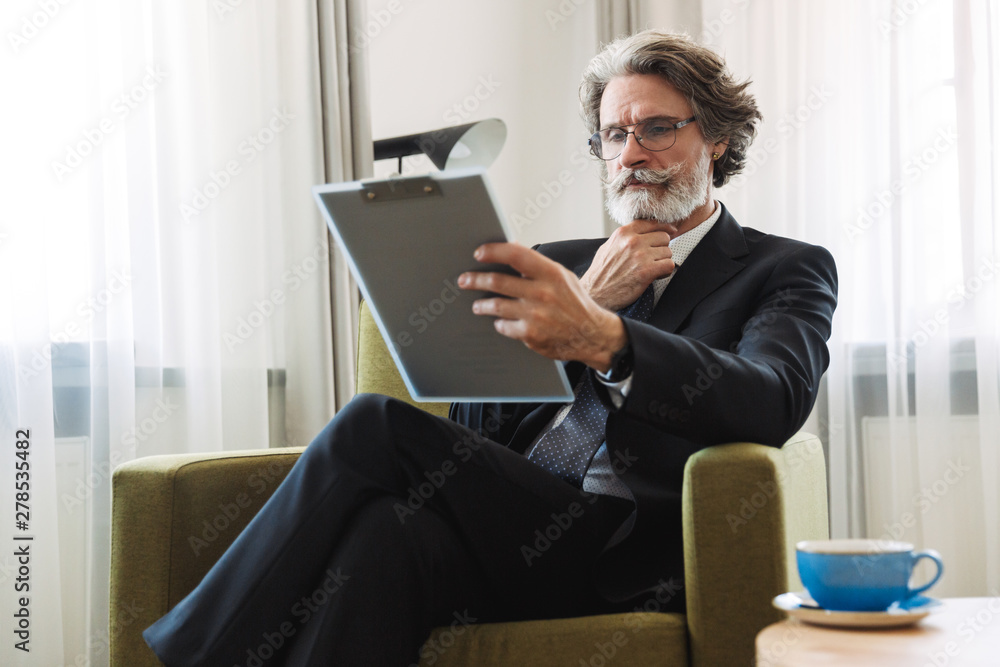 Portrait closeup of caucasian mature businessman holding clipboard while sitting on armchair in apartment Portrait closeup of caucasian mature businessman holding clipboard while sitting on armchair in apartment
