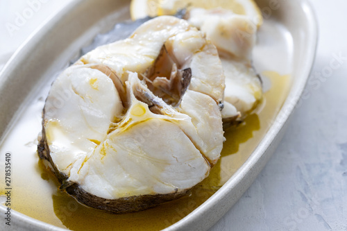 boiled fish with olive oil in dish on ceramic background