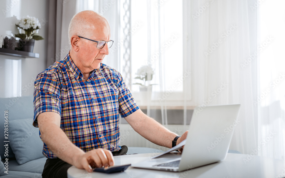 Senior male calculating bills using laptop at home Senior male calculating bills using laptop at home