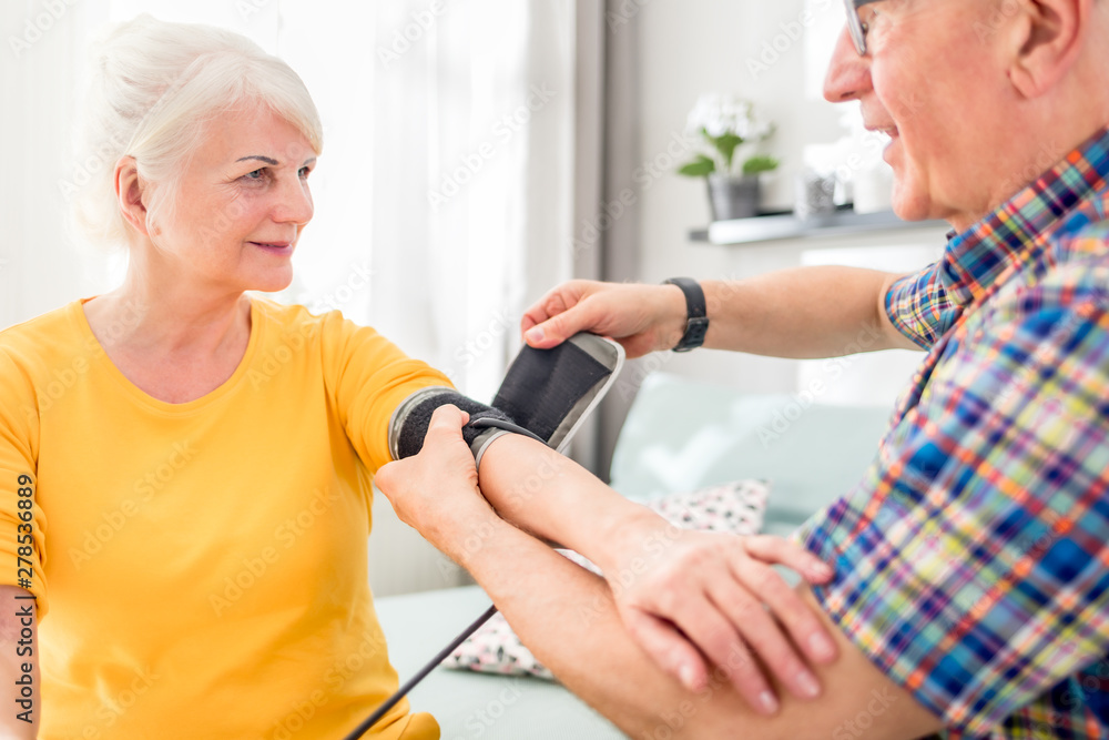 Senior husband doing blood pressure measurement to his wife at home Senior husband doing blood pressure measurement to his wife at home