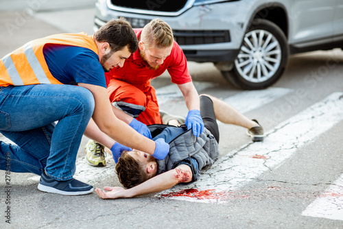 Fotografie Medic with car driver applying first aid to the injured man lying on the pedestr