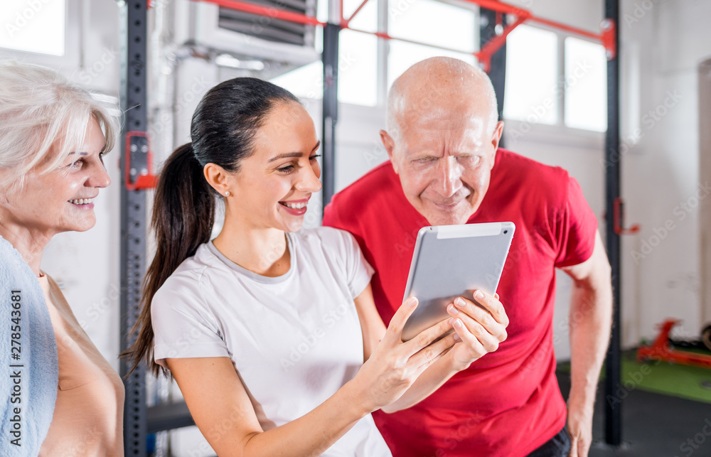 Personal trainer showing results of training on tablet to senior couple