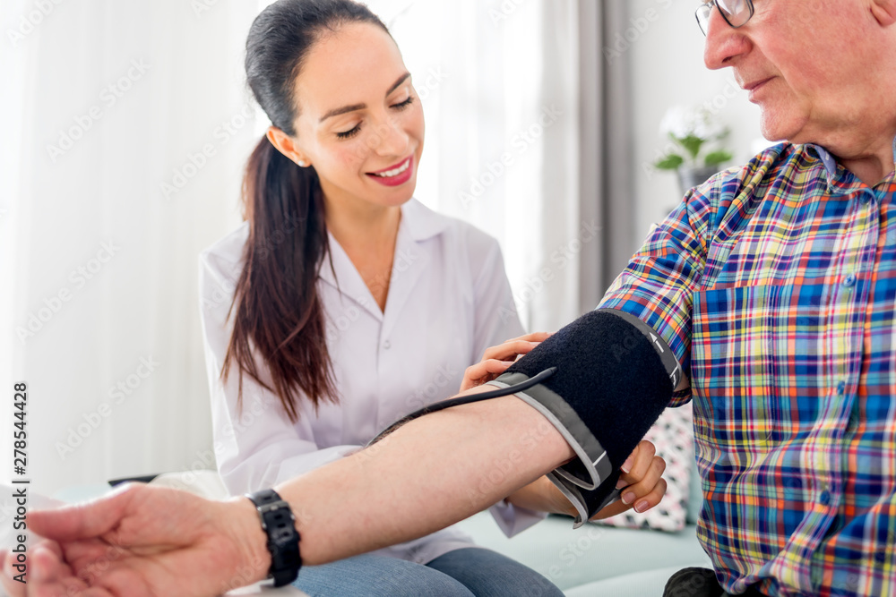 Nurse visiting senior male at home doing blood pressure measurement Nurse visiting senior male at home doing blood pressure measurement