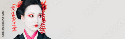 Quadro su tela beautiful geisha in black kimono with red flowers in hair looking away isolated