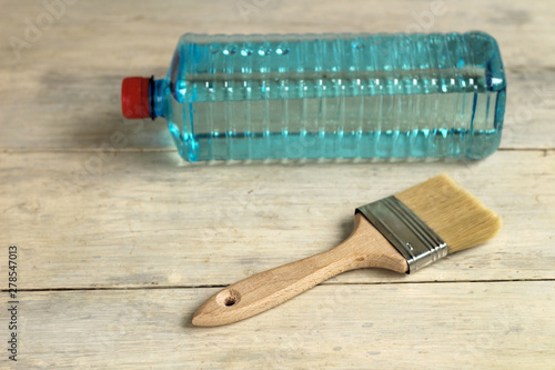 A brush lies next to a transparent plastic bottle with a solvent on an old white vintage wooden plank table. Place for text or logo. photo