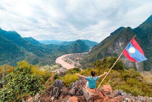 Woman with arms outstretched conquering mountain top at Nong Khiaw Nam Ou River valley Laos mature people traveling millenials concept travel destination in South East Asia