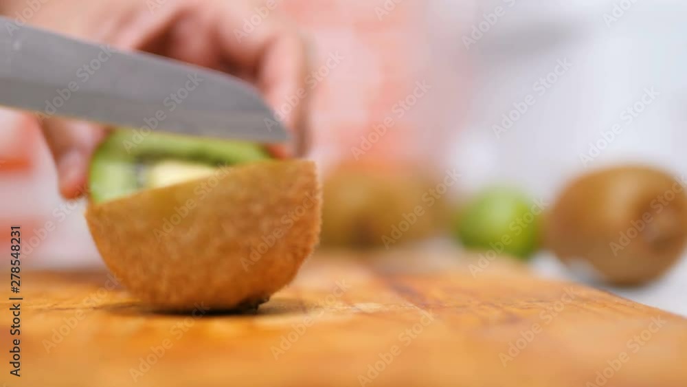 Hands of women using a knife sliced the kiwi fruit into pieces on wooden board in a kitchen Hands of women using a knife sliced the kiwi fruit into pieces on wooden board in a kitchen