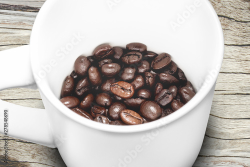 Roasted coffee beans in white cup and wood background